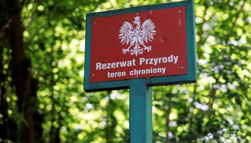 Tablica "Rezerwat Przyrody" z orłem w koronie, wskazująca na chroniony teren w dolinie Huczka.