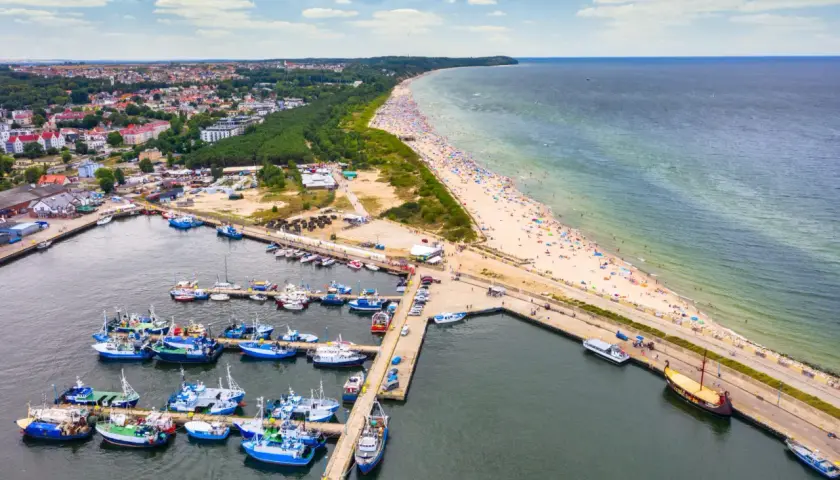 Port rybacki Władysławowo tętni życiem. Wiele łodzi cumuje, a plaża pełna jest wypoczywających.