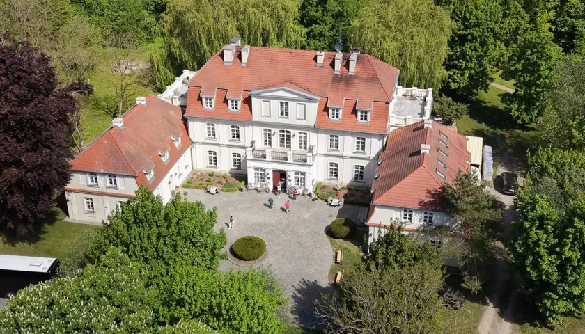 Piękny pałac Godętowo otoczony zielenią. Kilka osób spaceruje po dziedzińcu.