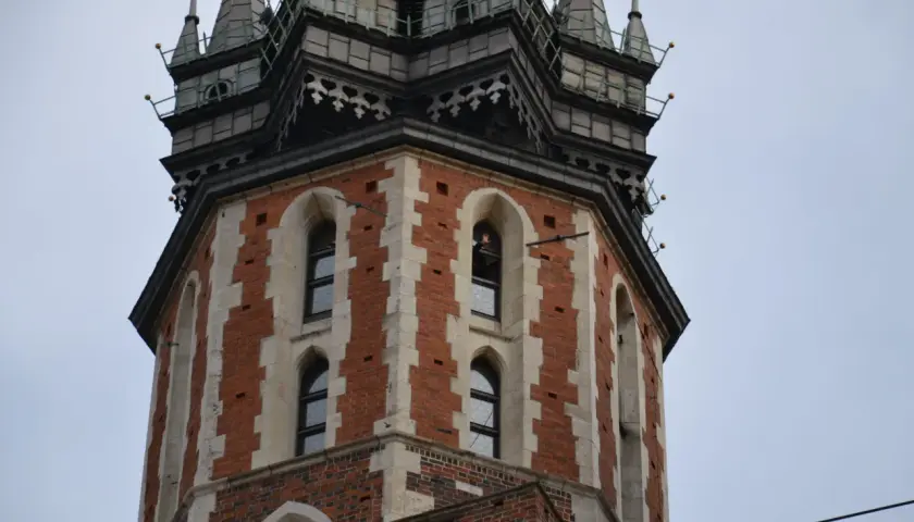 Wieża Kościoła Mariackiego w Krakowie, z cegły i kamienia, z charakterystycznymi oknami i zdobieniami.