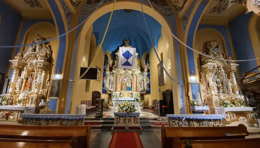 Wnętrze kościoła w Jastarni, bogato zdobiony ołtarz główny z figurami świętych, niebieskie sklepienie z gwiazdami i złote detale tworzą uroczystą atmosferę.