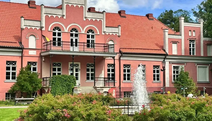 Pałac Przebendowskich w Wejherowie, różowy, z fontanną i kwitnącymi krzewami róż.
