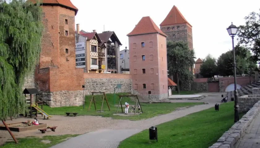 Wieże zamkowe w Chojnicach, Kaszuby, z placem zabaw i zielenią.