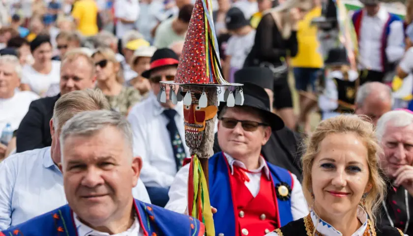 Stare i nowe brusy na festynie. Ludzie w tradycyjnych strojach, wśród nich mężczyzna z kolorową laską.