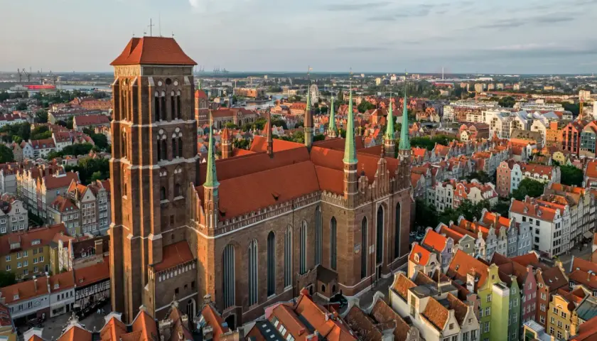 Majestatyczny kościół Mariacki w Gdańsku góruje nad miastem, otoczony kamienicami o czerwonych dachach.