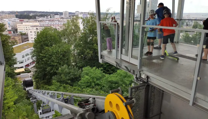 Dzieci na hulajnogach czekają na wjazd kolejką na kamienną górę w Gdyni, podziwiając panoramę miasta.