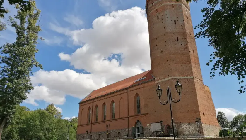 Chojnice zamek krzyżacki, ceglana wieża i budynek muzeum pod błękitnym niebem z chmurami.