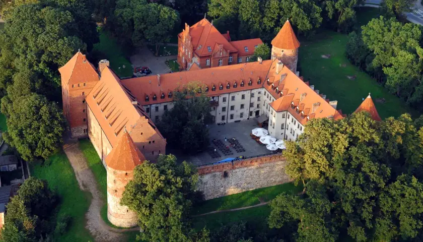 Zamek w Bytowie otoczony zielenią, z czerwonymi dachami i dziedzińcem.