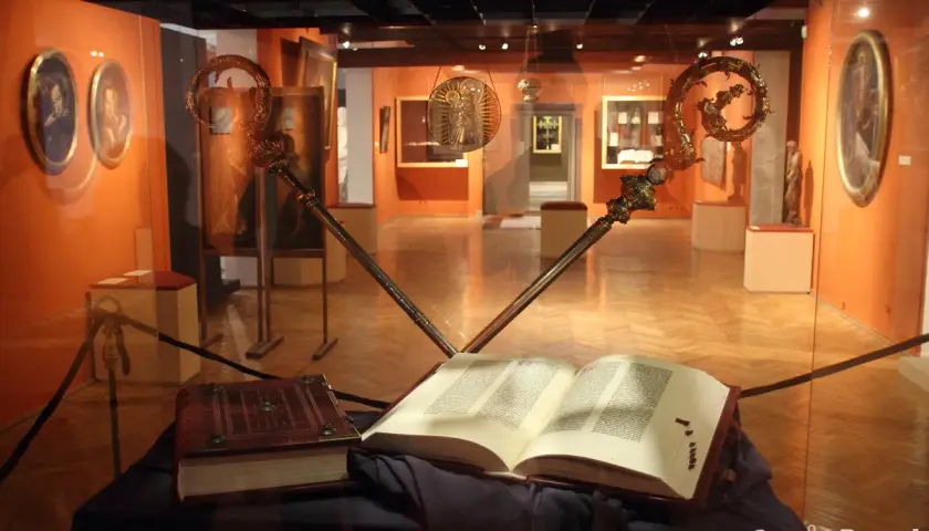 Otwarta biblia gutenberga pelplin, obok zamknięta księga i dwa ozdobne pastorały w muzeum.