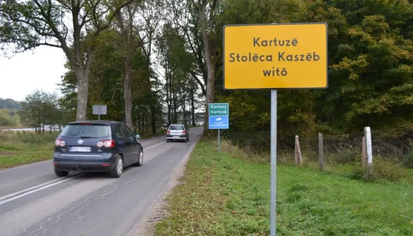 Żółty znak informuje: Kartuzë, Stolëca Kaszëb witô. Droga prowadzi do stolicy Kaszub.