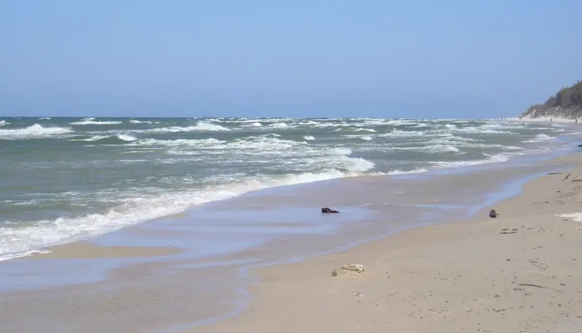 Plaża z falami i wydmami. W oddali widać ludzi spacerujących, co sugeruje, że to miejsce oferuje ciekawe **rowy atrakcje**.