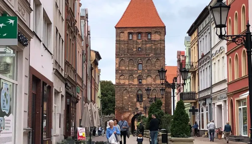 Spacer po urokliwej uliczce z kolorowymi kamienicami, w tle majestatyczna brama człuchowska.