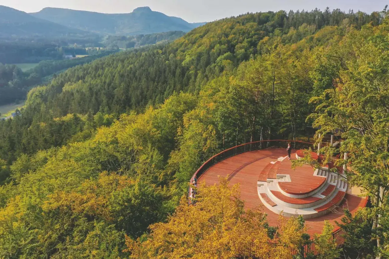 Drewniane wierze widokowe z amfiteatrem otoczone jesiennym lasem. W oddali góry i dolina.