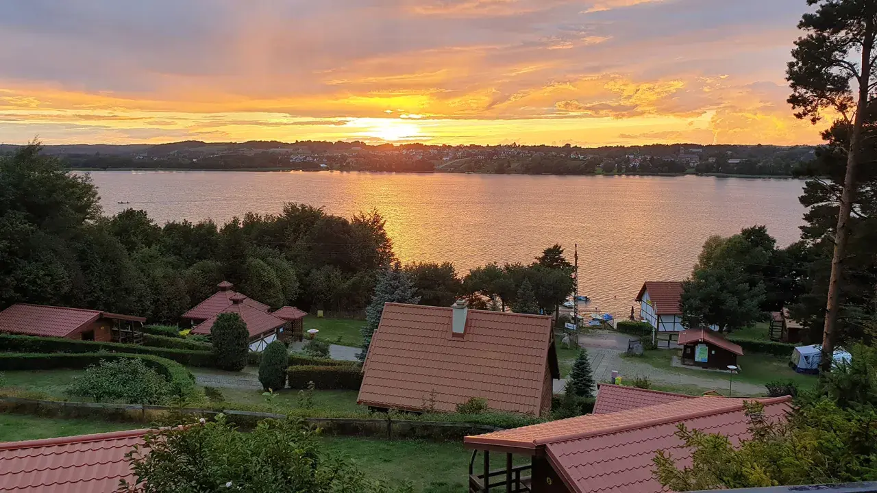 Zachód słońca nad jeziorem, domki letniskowe i zieleń. Tamowa Chmielno w złotej poświacie.
