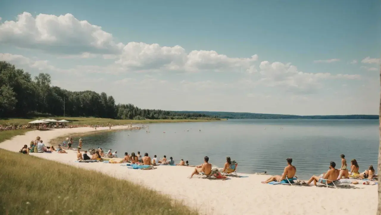 Ludzie odpoczywają na piaszczystej plaży w **Ostrzyce Park**. Woda jest spokojna, a niebo błękitne z białymi chmurami.