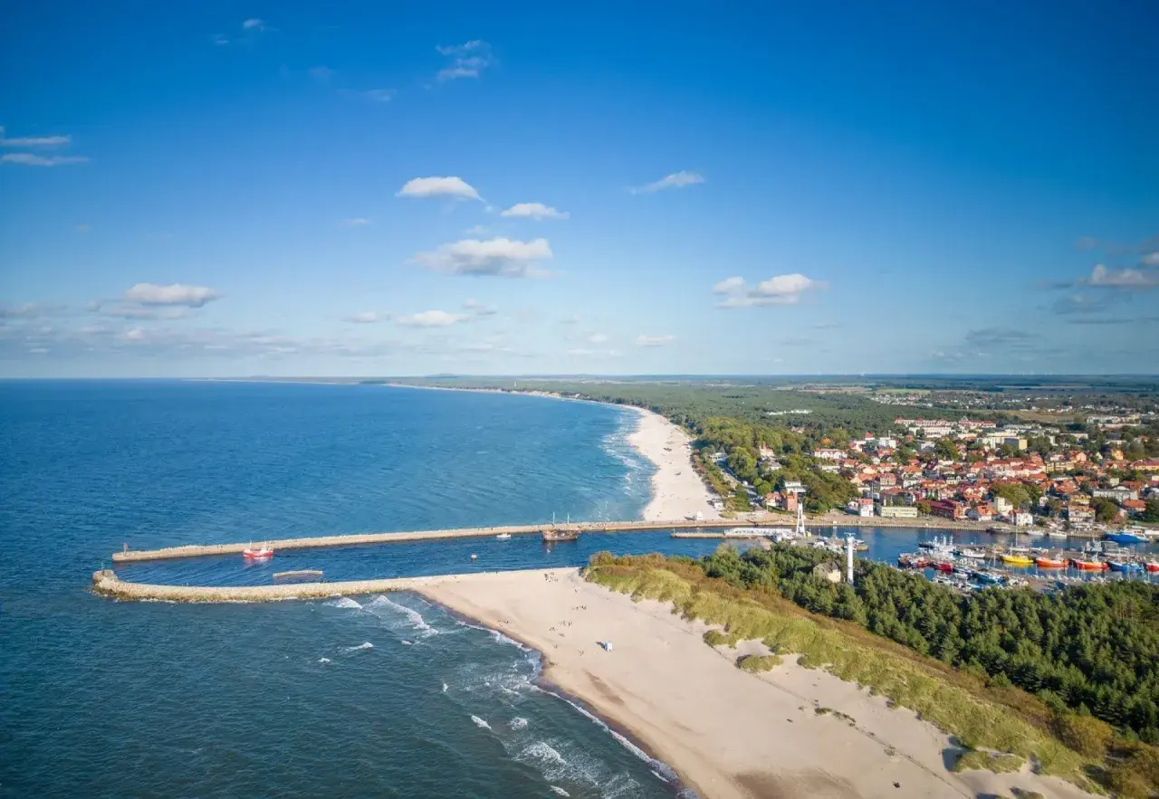 Malownicza plaża w Ustce z widokiem na port, morze i miasto. Słoneczny dzień zachęca do wypoczynku.