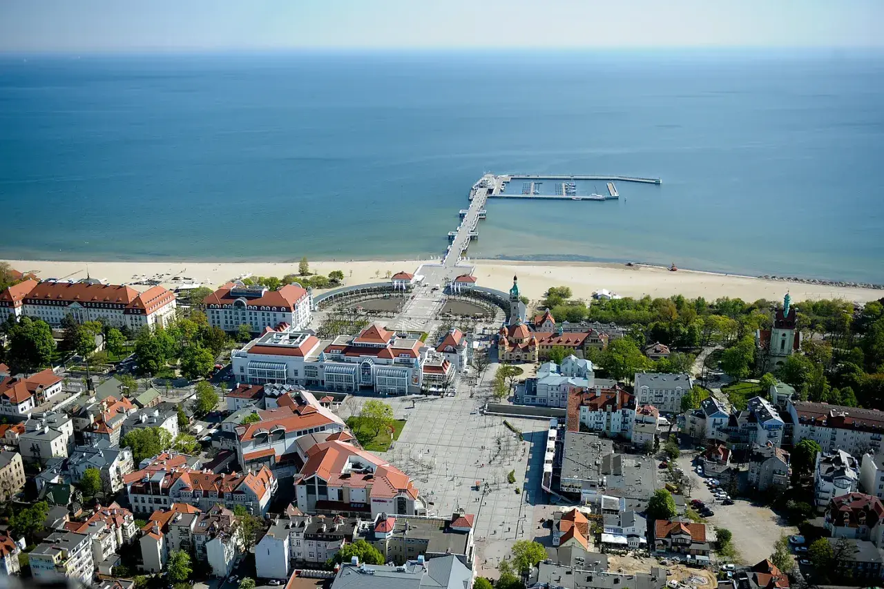 Widok na Sopot, część Trójmiasta. Widoczny deptak, plaża, molo i budynki z czerwonymi dachami.