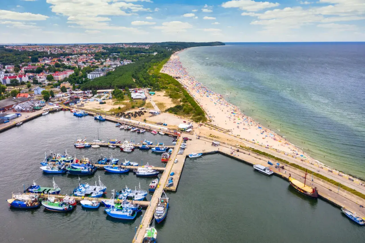 Port rybacki Władysławowo tętni życiem. Wiele łodzi cumuje, a plaża pełna jest wypoczywających.