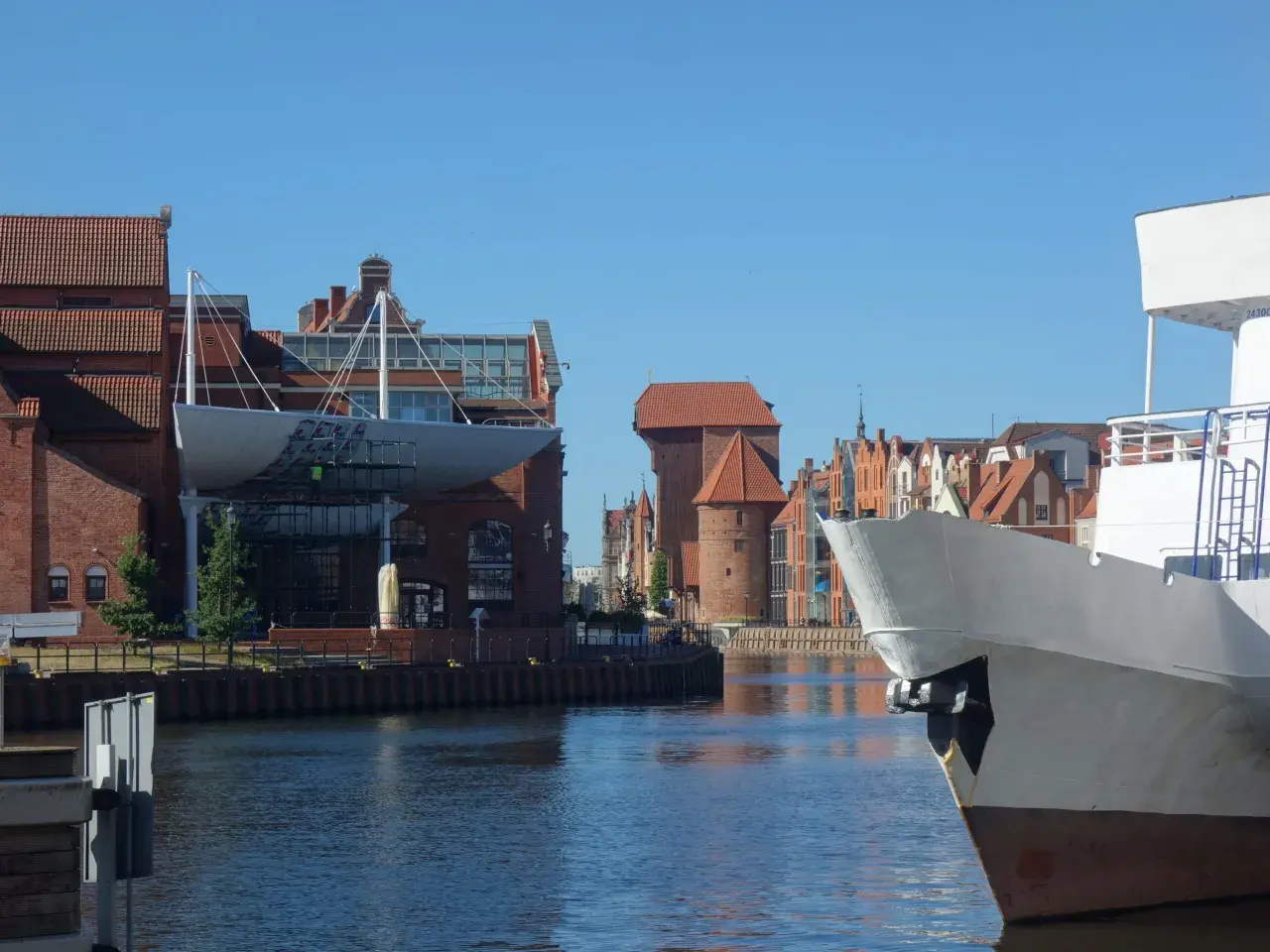 Widok na Motławę w Gdańsku. Na pierwszym planie biały dziób statku, w tle zabytkowe kamienice i Żuraw. Gdańsk starówka zachwyca.