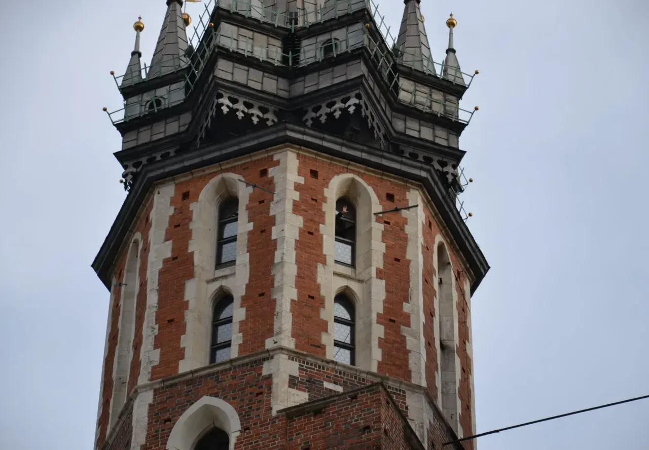 Wieża Kościoła Mariackiego w Krakowie, z cegły i kamienia, z charakterystycznymi oknami i zdobieniami.