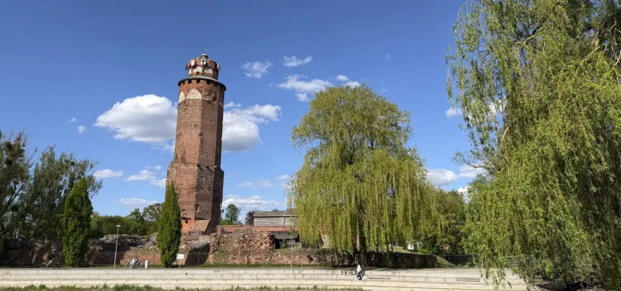 Wieża w Brodnicy Górnej, otoczona zielenią i ruinami, pod błękitnym niebem z chmurami.