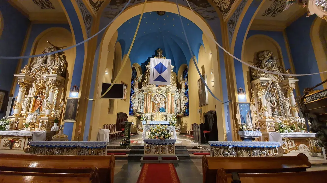 Wnętrze kościoła w Jastarni, bogato zdobiony ołtarz główny z figurami świętych, niebieskie sklepienie z gwiazdami i złote detale tworzą uroczystą atmosferę.