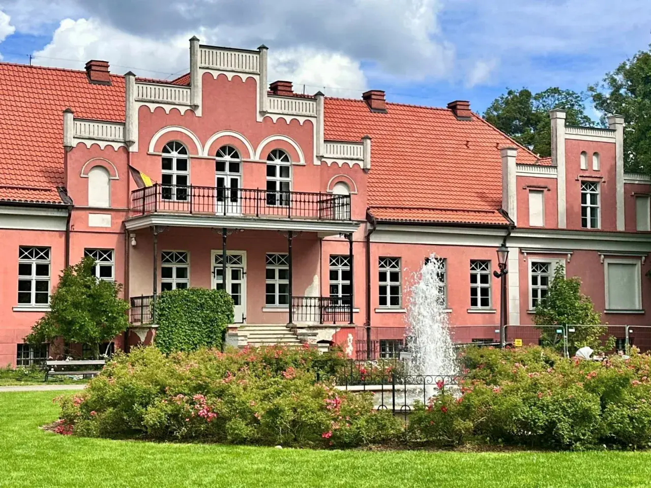 Pałac Przebendowskich w Wejherowie, różowy, z fontanną i kwitnącymi krzewami róż.
