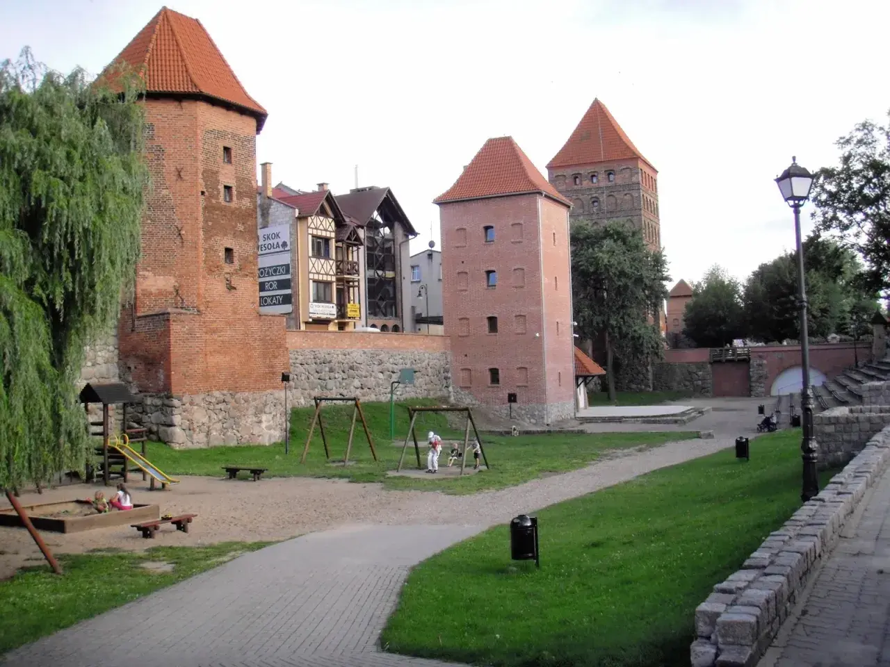 Wieże zamkowe w Chojnicach, Kaszuby, z placem zabaw i zielenią.