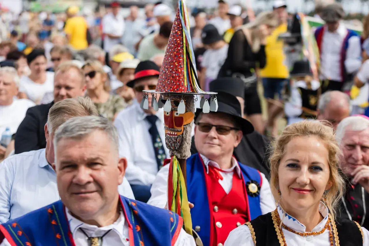 Stare i nowe brusy na festynie. Ludzie w tradycyjnych strojach, wśród nich mężczyzna z kolorową laską.
