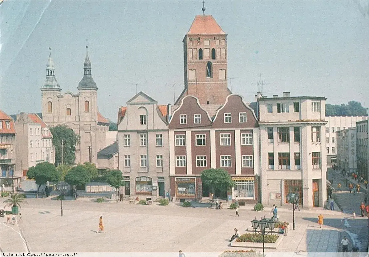 Chojnice rynek z kościołem i kamienicami. Ludzie spacerują po placu, tworząc tętniące życiem tło dla zabytkowej architektury.