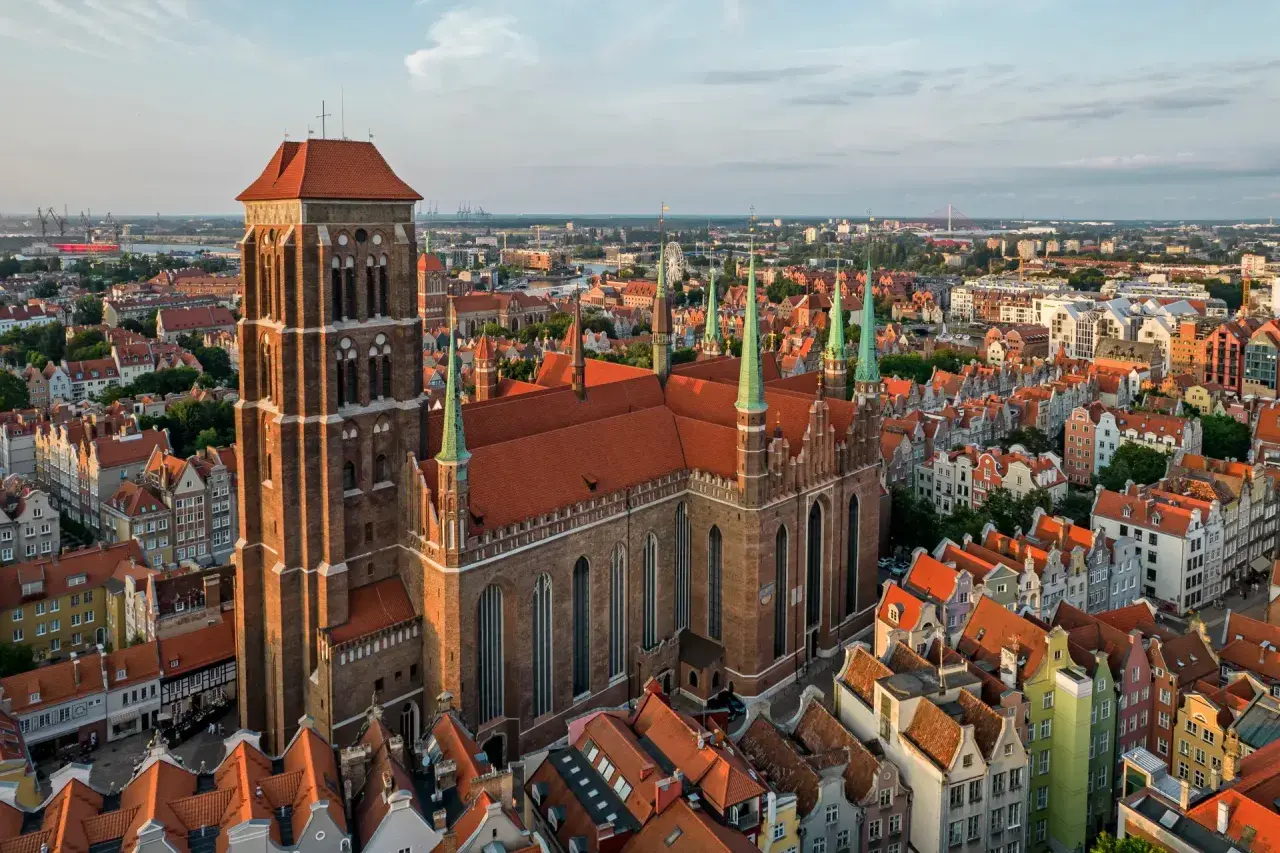 Majestatyczny kościół Mariacki w Gdańsku góruje nad miastem, otoczony kamienicami o czerwonych dachach.