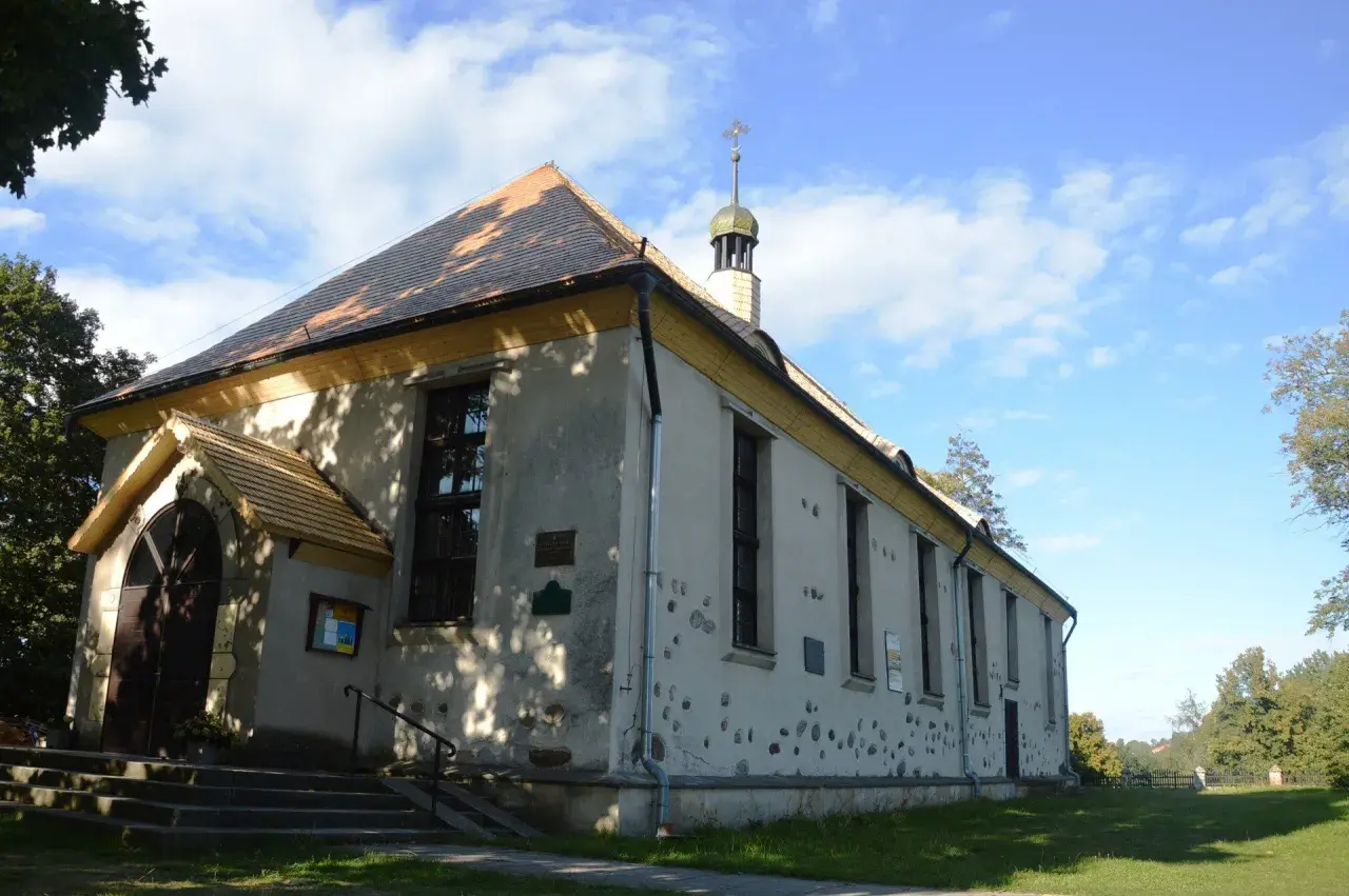 Cerkiew w Bytach, prosta budowla z charakterystycznym dachem i wieżyczką, otoczona zielenią.