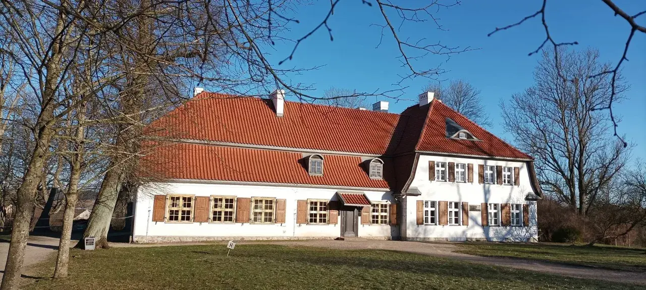 Dworek Wybickich z czerwonym dachem i białymi ścianami, otoczony nagimi drzewami, w słoneczny dzień.