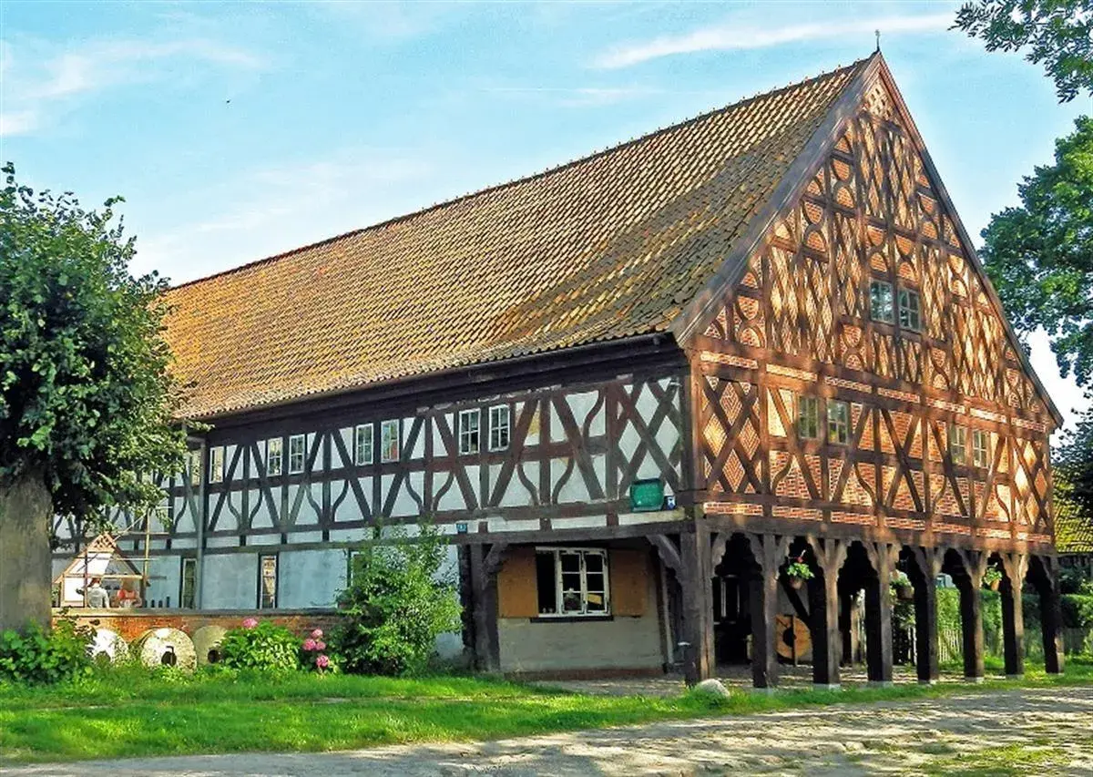 Drewniany dom podcieniowy, część szlaku mennonitów, z charakterystyczną kratownicą i ceramicznym dachem.
