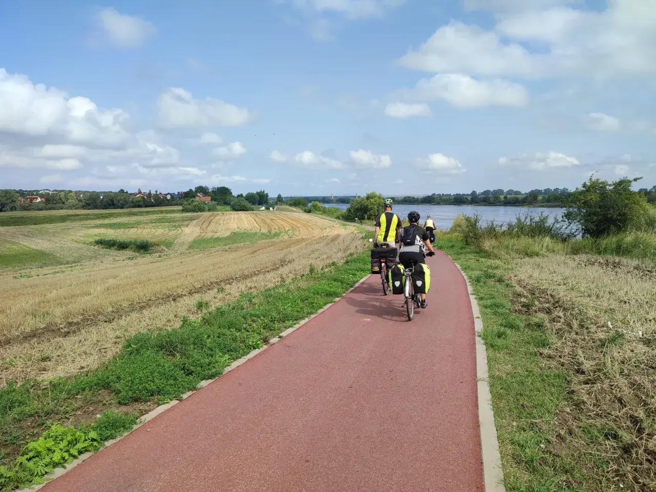 Rowerzyści na tczewskiej trasie podziwiają krajobraz z polami i rzeką.