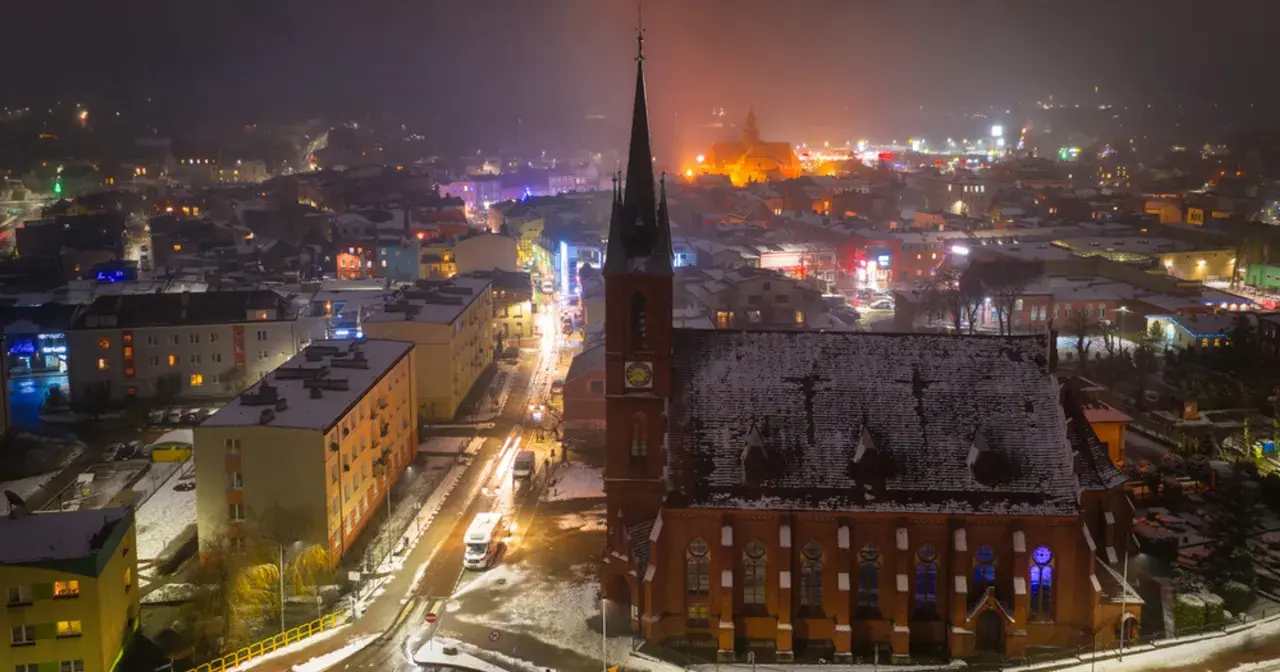 Nocna panorama Kościerzyny zimową porą. Widać ośnieżony kościół, oświetloną ulicę i kolorowe budynki. To piękne kościerzyna atrakcje.
