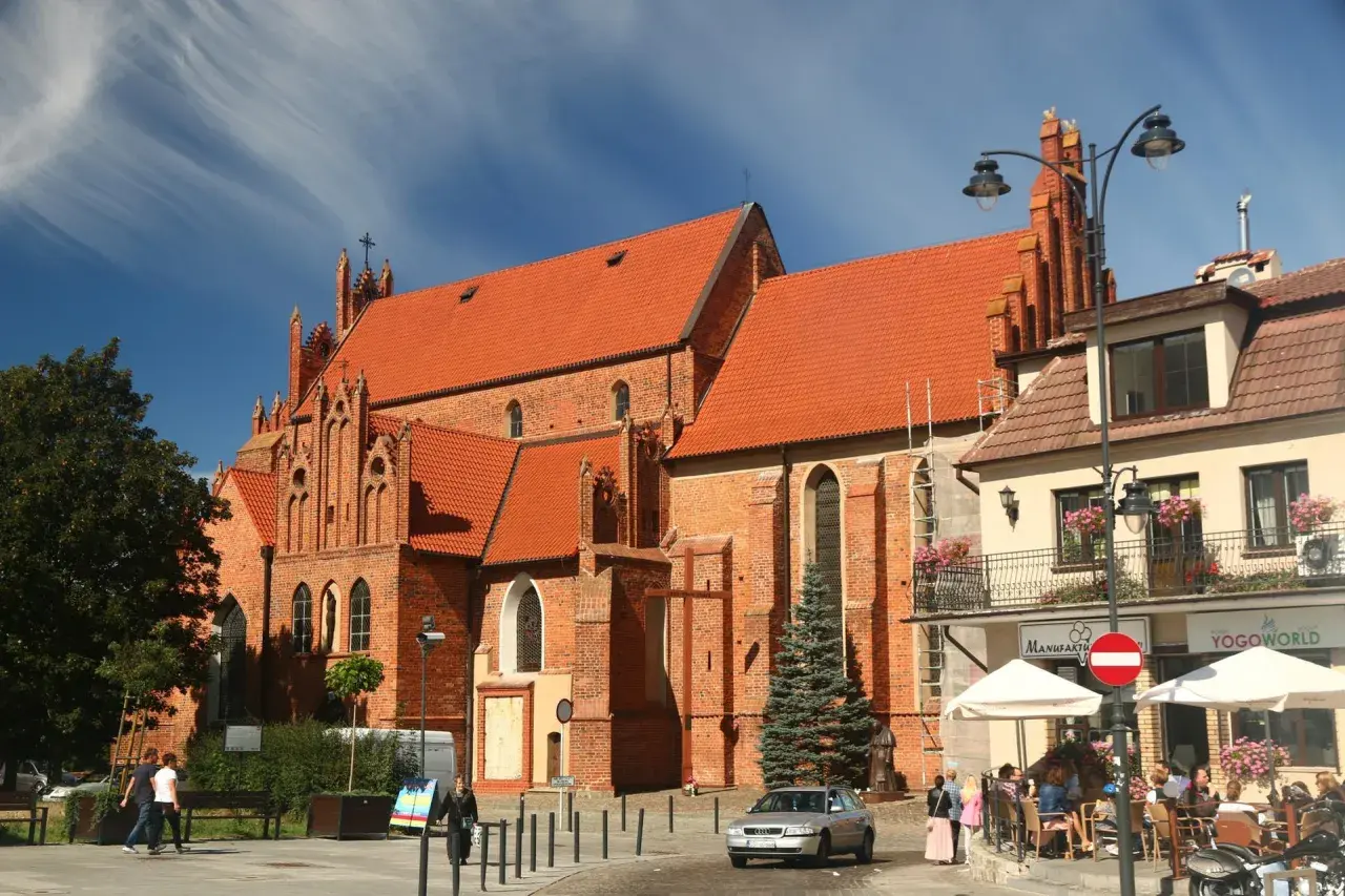 Starogard Gdański atrakcje: ceglana bazylika z czerwonym dachem i gotyckimi detalami, plac z kawiarnią i ludźmi.