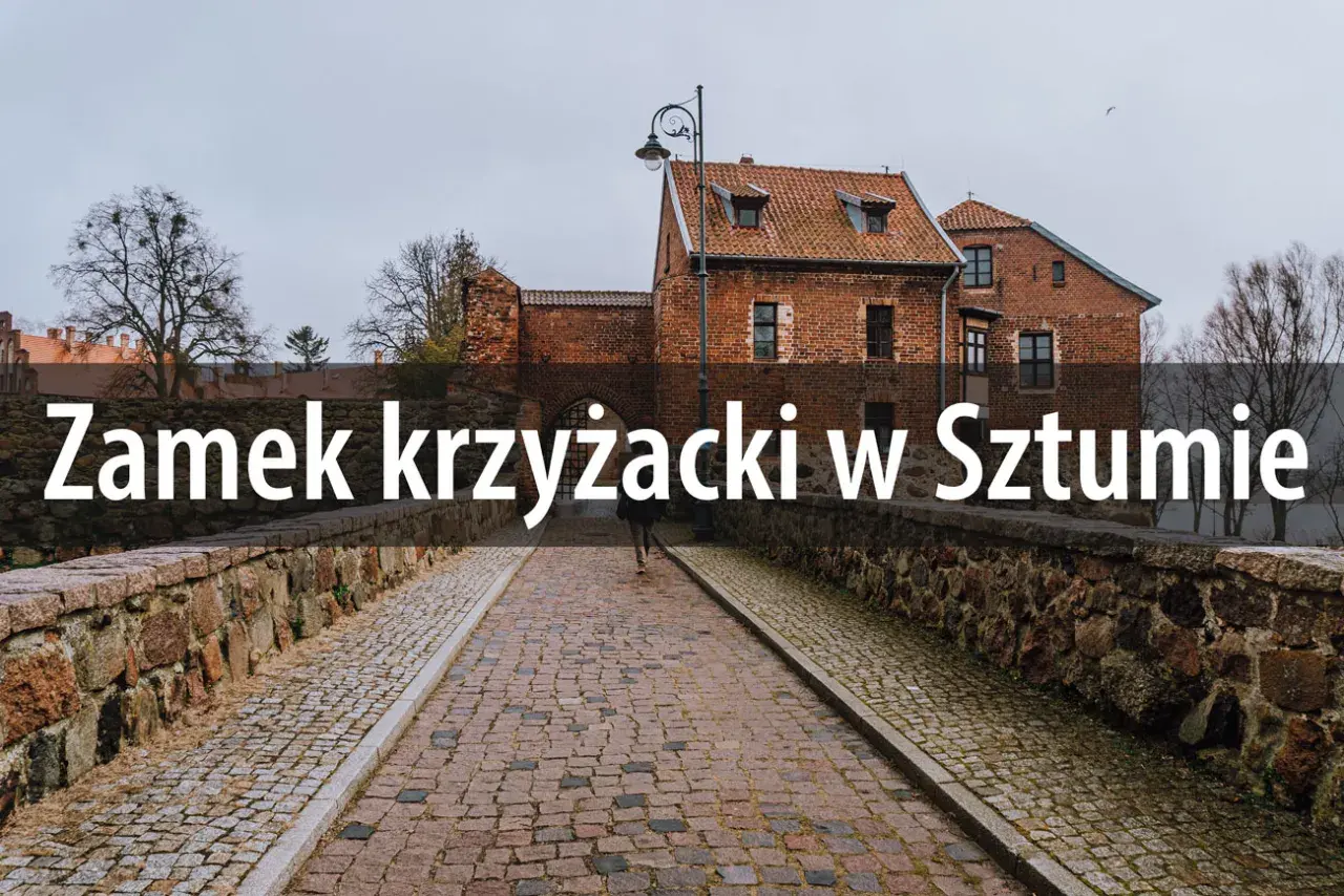 Kamienny most prowadzi do ceglanego zamku krzyżackiego w Sztumie. W oddali widać drzewa i pochmurne niebo.