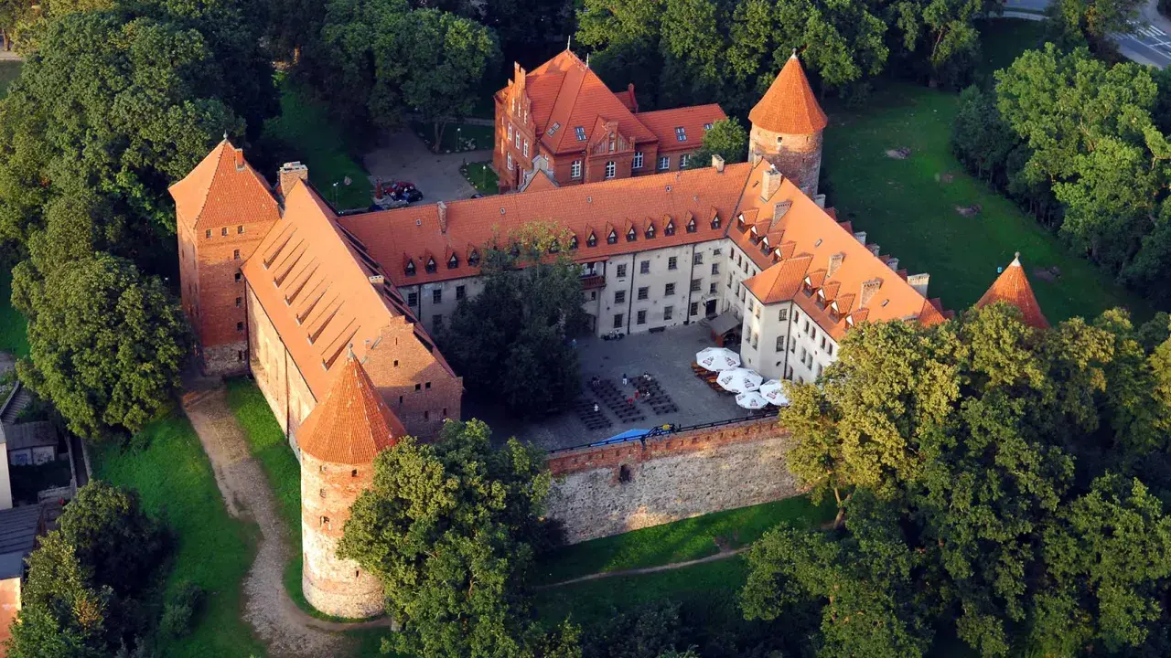 Zamek w Bytowie otoczony zielenią, z czerwonymi dachami i dziedzińcem.
