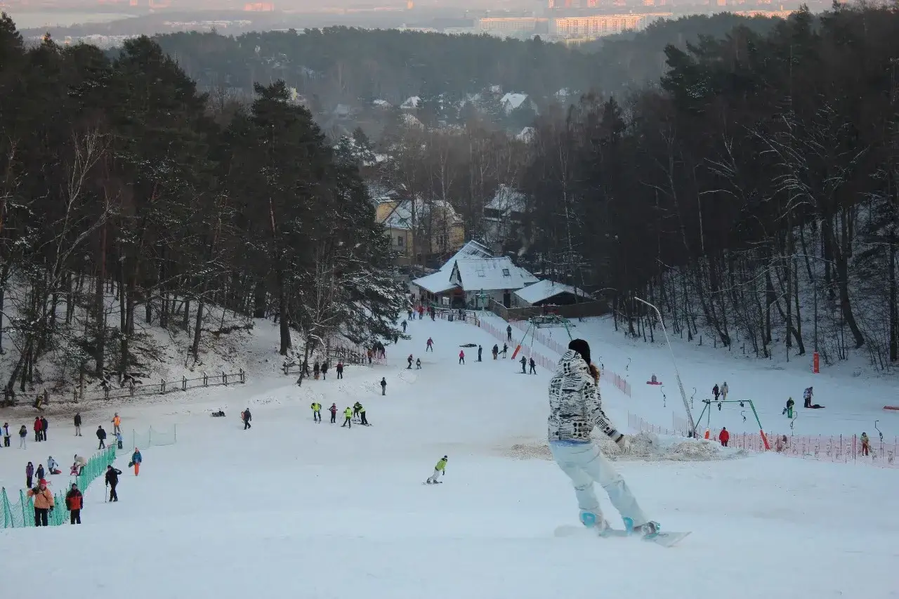 Zimowy stok narciarski w Sopocie, z widokiem na miasto w oddali. Ludzie jeżdżą na nartach i snowboardach.