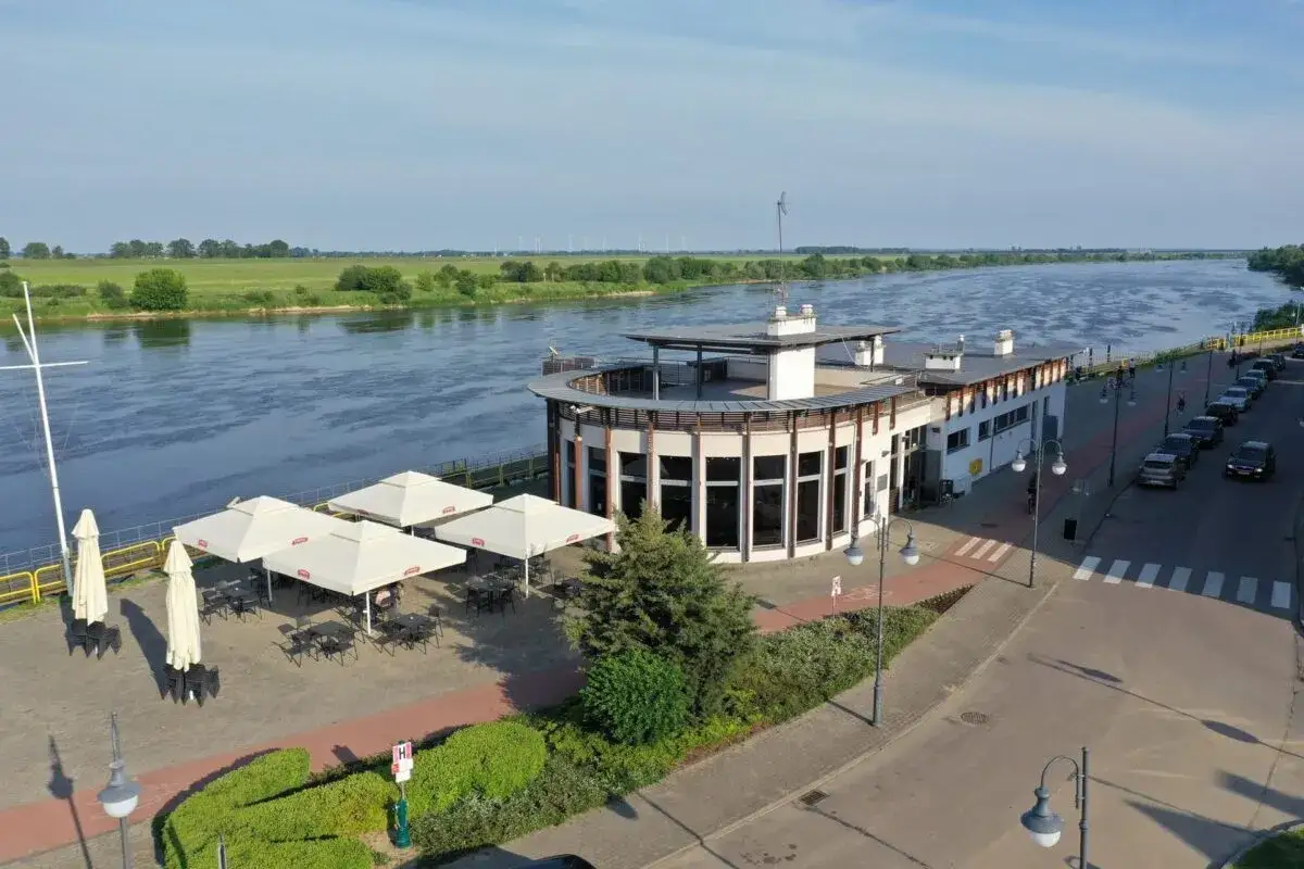 Tczew atrakcje: nowoczesny budynek nad Wisłą z tarasem i ogródkiem letnim, otoczony zielenią i promenadą.