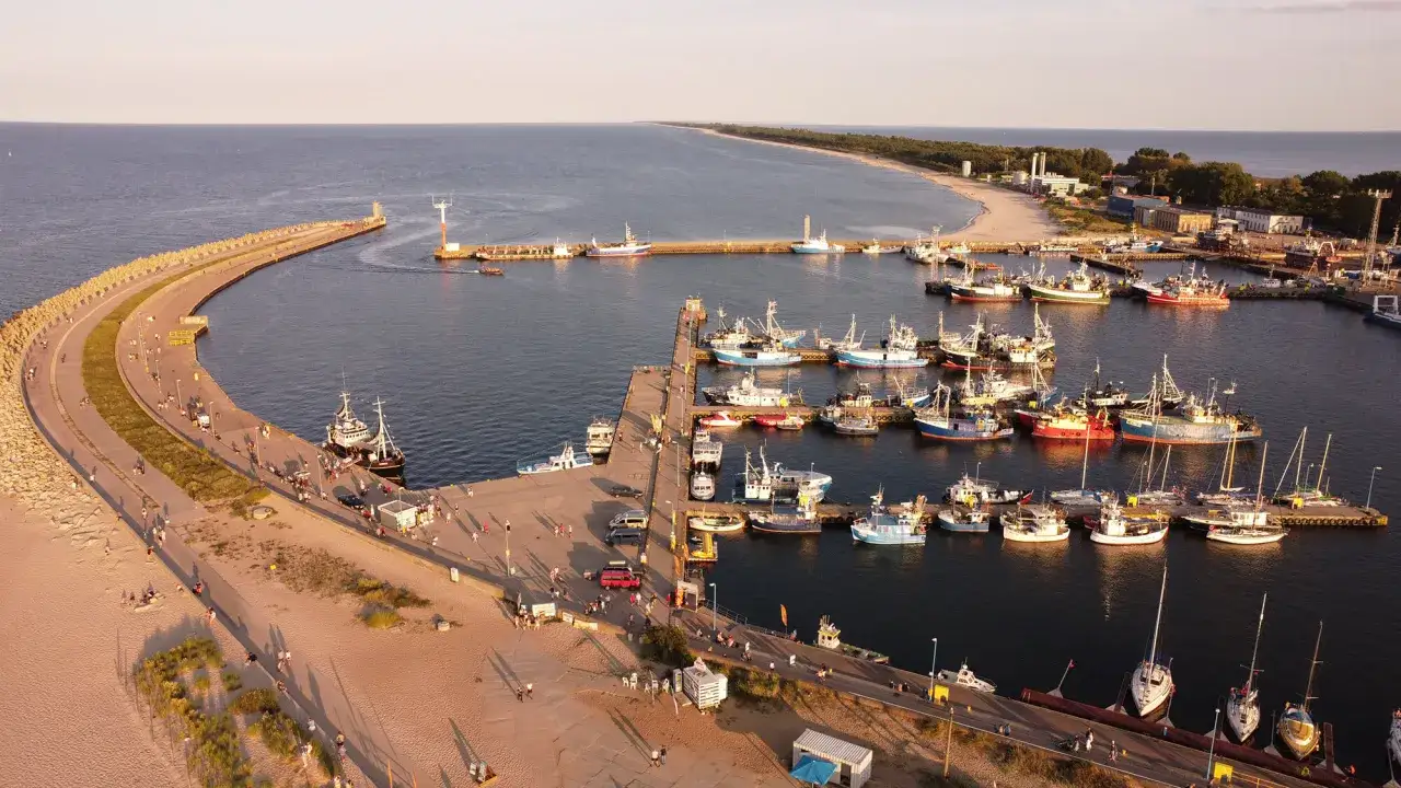 Władysławowo co zobaczyć: port rybacki z łodziami, molo, plaża i latarnia morska.