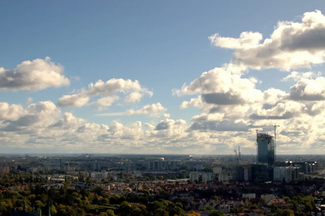 Widok z punktu widokowego Pachołek na miasto pod chmurami. Widać nowoczesny wieżowiec w budowie i rozległą panoramę zabudowań.