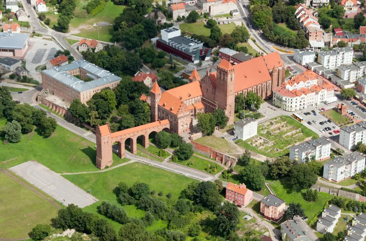 Widok z lotu ptaka na zamek w Kwidzynie z charakterystycznym gdaniskiem i mostem. Otoczony zielenią i zabudowaniami miejskimi.