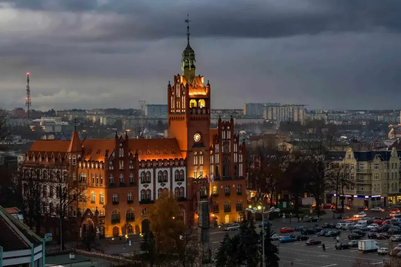 Wieczorny widok na ratusz w Słupsku, jedną z głównych atrakcji miasta. Budynek oświetlony, otoczony zabudową miejską.
