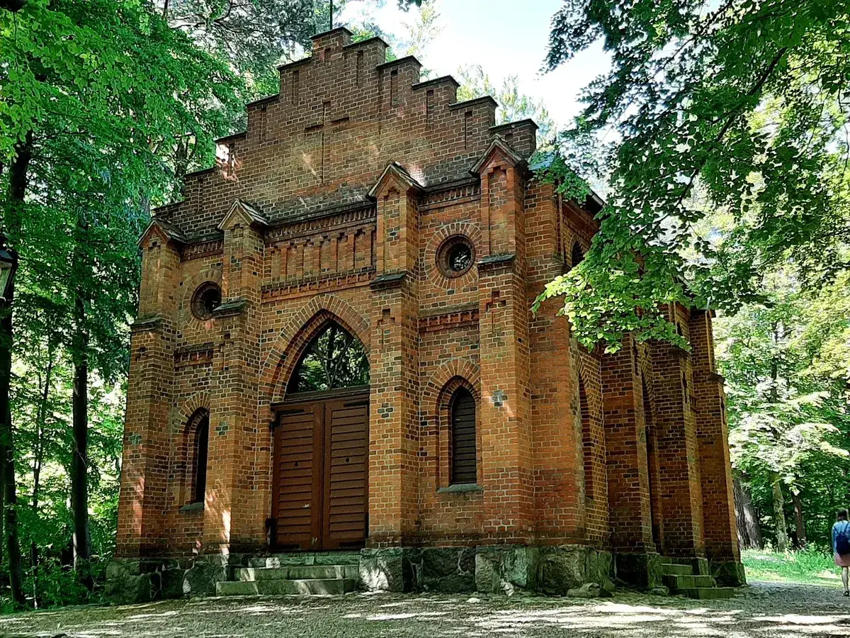 Gotycki kościół z cegły w Wejherowie, otoczony zielenią.
