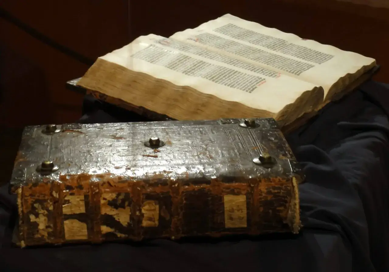 Dwie księgi: zamknięta, zabytkowa biblia gutenberga pelplin z metalowymi okuciami i otwarta, z tekstem.