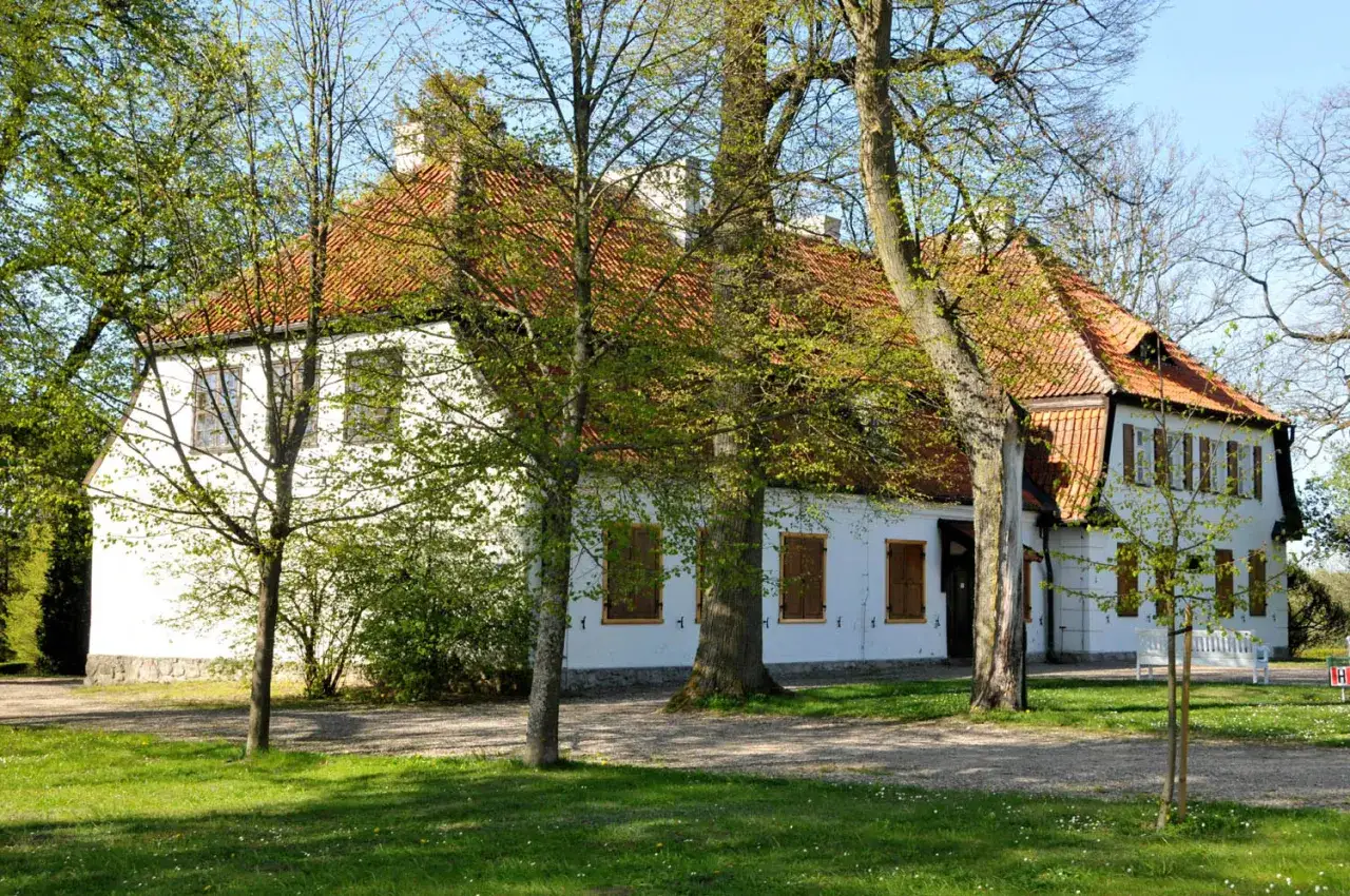 Biały dworek z czerwonym dachem, otoczony zielenią. To dworek Wybickich, miejsce pełne historii i spokoju.