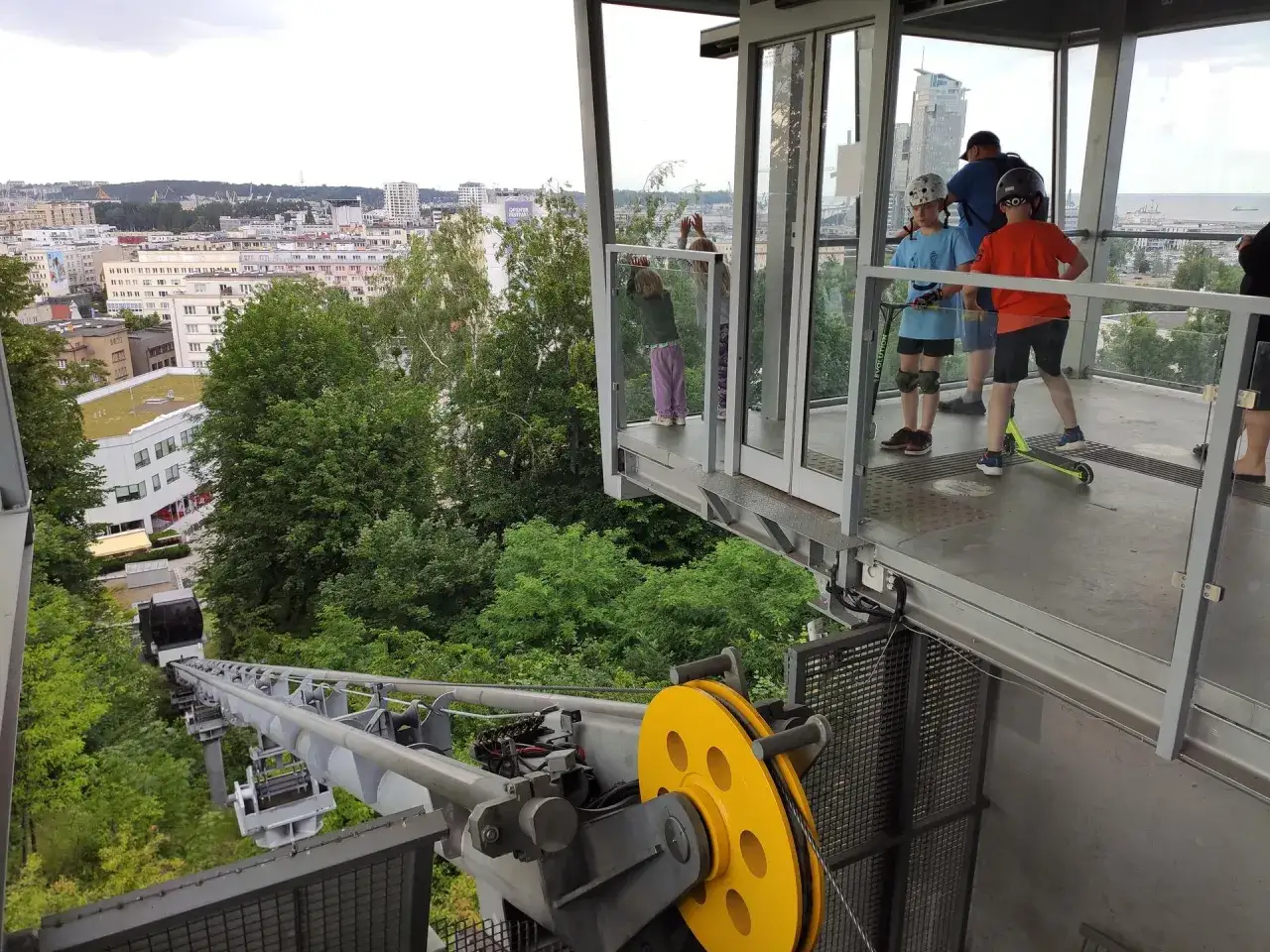 Dzieci na hulajnogach czekają na wjazd kolejką na kamienną górę w Gdyni, podziwiając panoramę miasta.