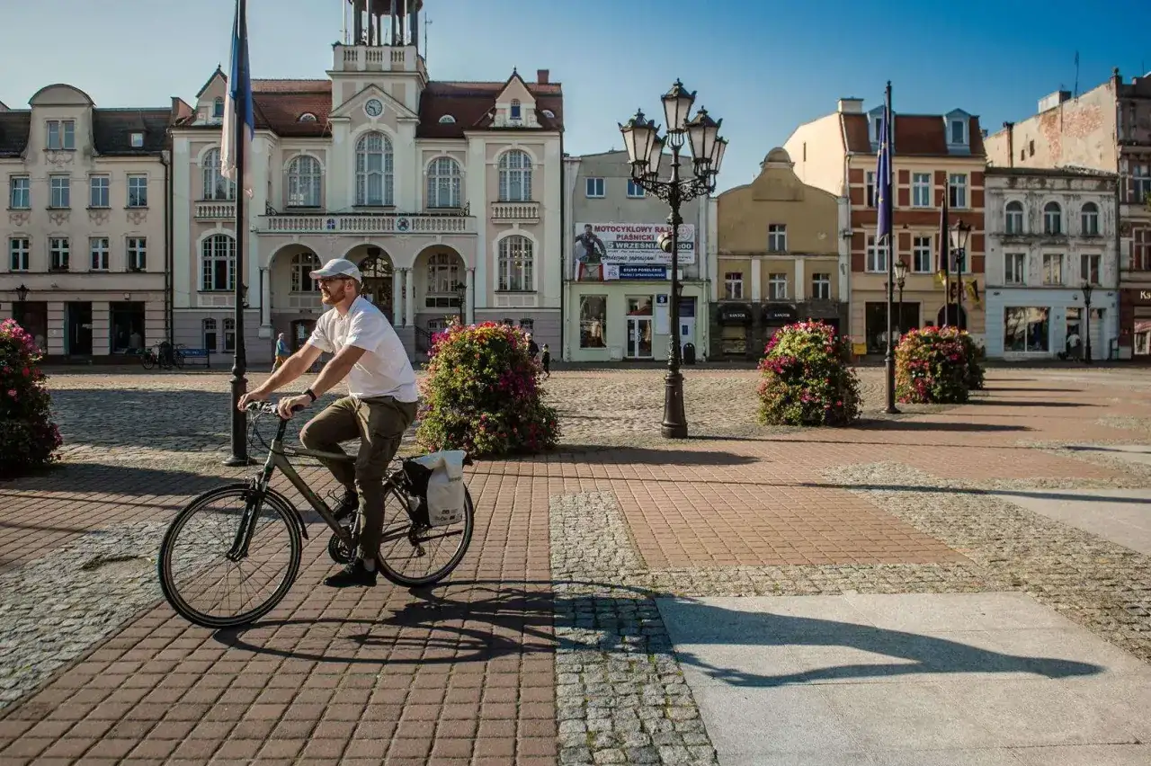 Mężczyzna na rowerze przemierza urokliwą trasę w Wejherowie, mijając zabytkowe kamienice i kwitnące krzewy.